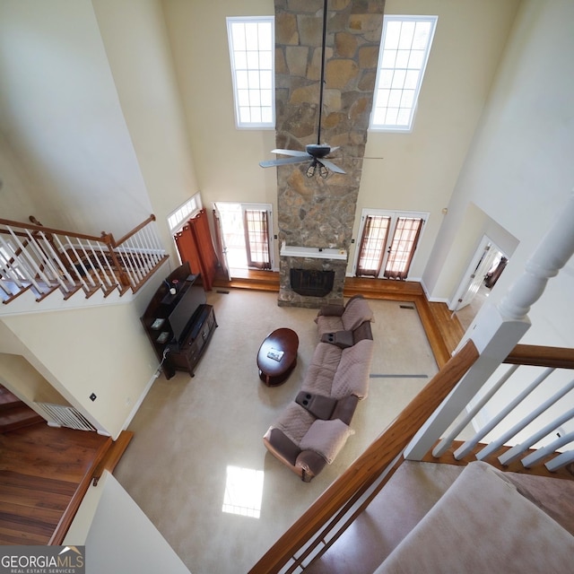 living room with ceiling fan, carpet flooring, a fireplace, and a high ceiling