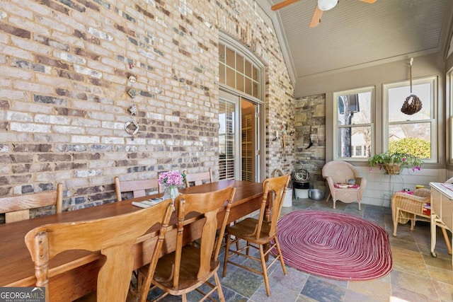 dining space featuring ceiling fan, brick wall, and high vaulted ceiling