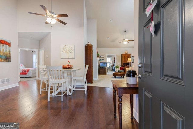 dining space with dark hardwood / wood-style floors, ceiling fan, and a towering ceiling