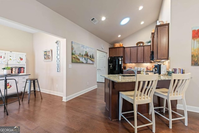 kitchen with sink, a breakfast bar area, light stone counters, black fridge with ice dispenser, and dark wood-type flooring