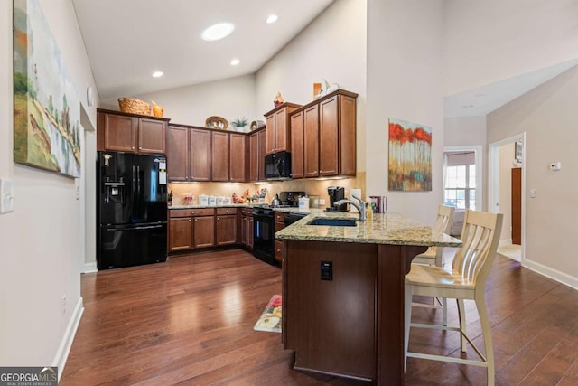 kitchen with black appliances, sink, a breakfast bar area, kitchen peninsula, and light stone countertops