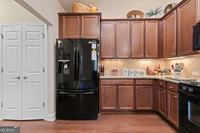 kitchen featuring light stone counters, wood-type flooring, tasteful backsplash, and black appliances