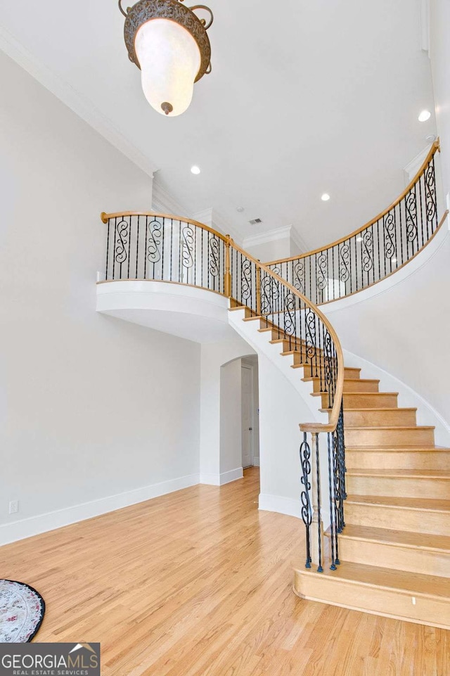 staircase featuring hardwood / wood-style flooring, ornamental molding, and a towering ceiling