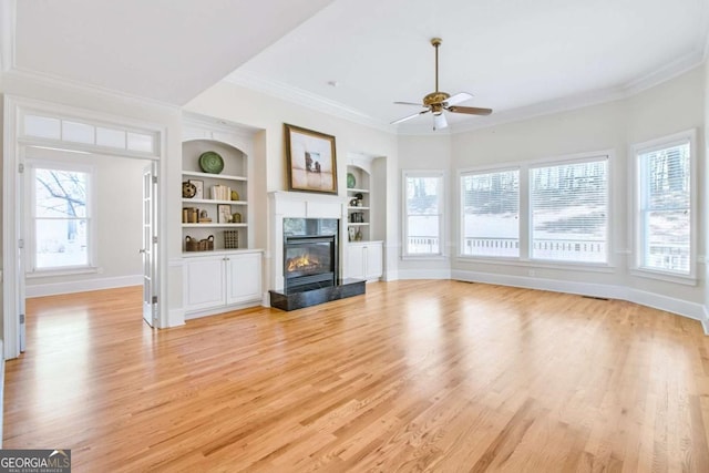 unfurnished living room with ornamental molding, light wood-type flooring, built in features, and a high end fireplace