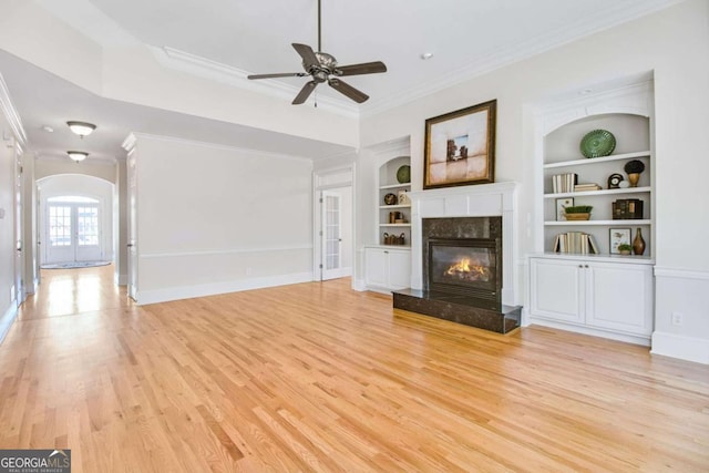 unfurnished living room featuring a premium fireplace, ornamental molding, built in features, and light hardwood / wood-style floors