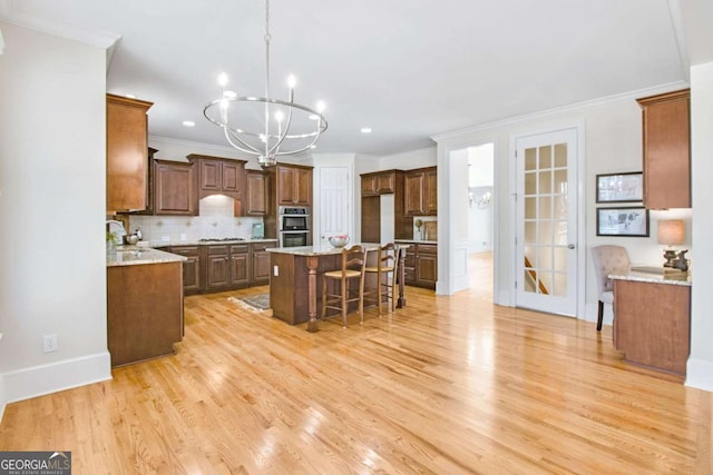 kitchen with a kitchen bar, a center island, light wood-type flooring, a notable chandelier, and decorative backsplash