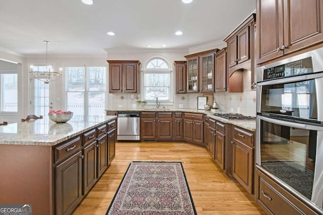 kitchen with a kitchen island, appliances with stainless steel finishes, sink, ornamental molding, and light wood-type flooring