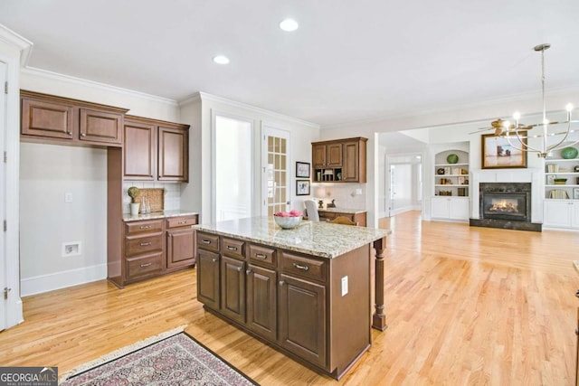 kitchen featuring pendant lighting, light stone counters, ornamental molding, light hardwood / wood-style floors, and a kitchen island