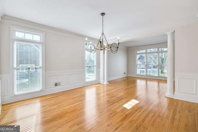 unfurnished dining area featuring decorative columns, crown molding, hardwood / wood-style flooring, and a chandelier