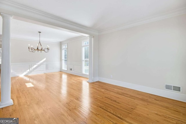 spare room featuring a notable chandelier, crown molding, light hardwood / wood-style flooring, and decorative columns