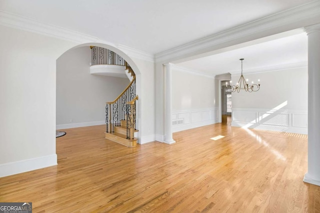 unfurnished living room with crown molding, hardwood / wood-style flooring, a chandelier, and ornate columns