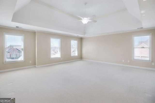 empty room featuring a raised ceiling, crown molding, light carpet, and ceiling fan