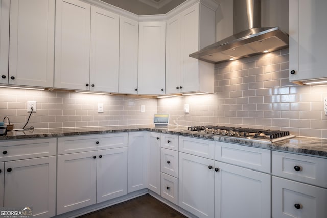 kitchen featuring wall chimney exhaust hood, tasteful backsplash, white cabinets, dark stone counters, and stainless steel gas stovetop