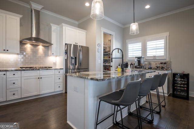 kitchen with stainless steel appliances, a kitchen island with sink, white cabinets, and wall chimney exhaust hood