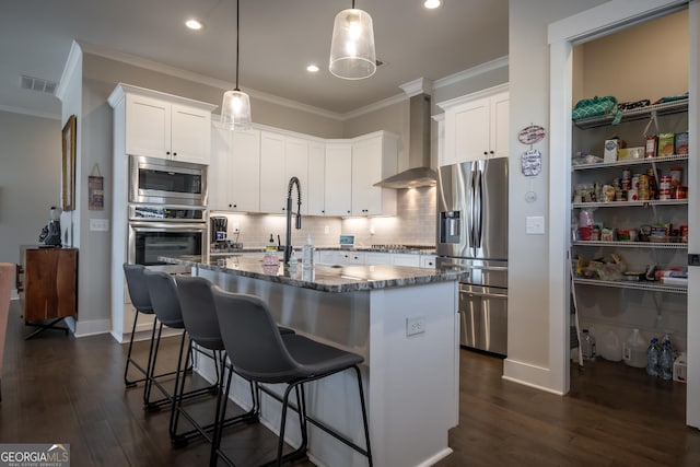 kitchen featuring white cabinetry, wall chimney range hood, an island with sink, and appliances with stainless steel finishes