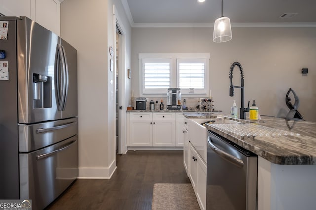 kitchen featuring crown molding, appliances with stainless steel finishes, white cabinets, decorative light fixtures, and dark stone counters