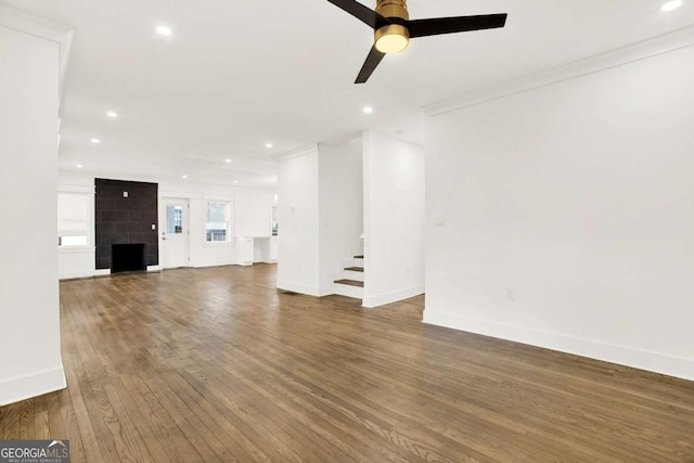 unfurnished living room featuring ceiling fan, a large fireplace, crown molding, and dark hardwood / wood-style flooring