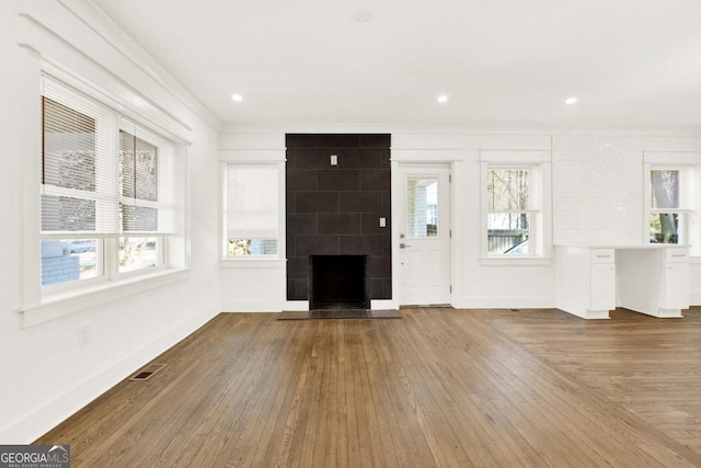 unfurnished living room with crown molding, wood-type flooring, a fireplace, and plenty of natural light