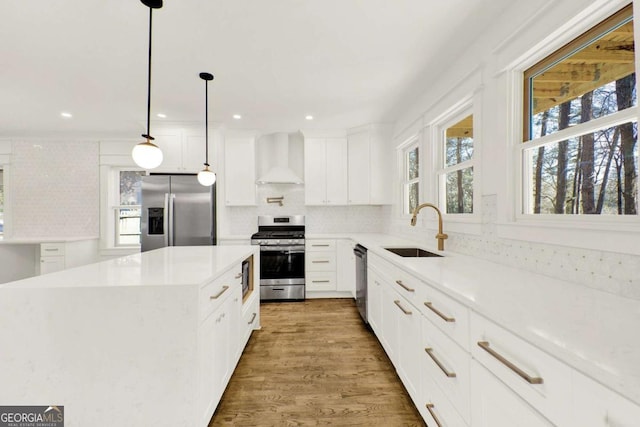 kitchen featuring sink, wall chimney range hood, white cabinetry, hanging light fixtures, and stainless steel appliances