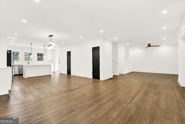 unfurnished living room with dark wood-type flooring, crown molding, and ceiling fan with notable chandelier