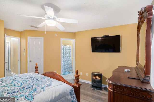 bedroom with ceiling fan, light hardwood / wood-style floors, a textured ceiling, and a wood stove