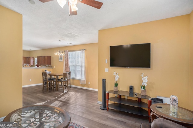 living room with dark wood-type flooring, ceiling fan with notable chandelier, and a textured ceiling