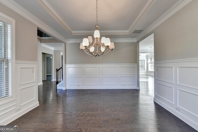 unfurnished dining area featuring a raised ceiling, crown molding, dark wood-type flooring, and an inviting chandelier