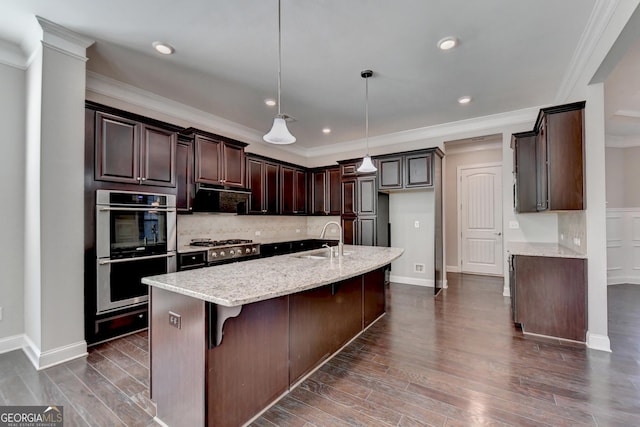 kitchen with pendant lighting, double oven, sink, a kitchen island with sink, and light stone countertops