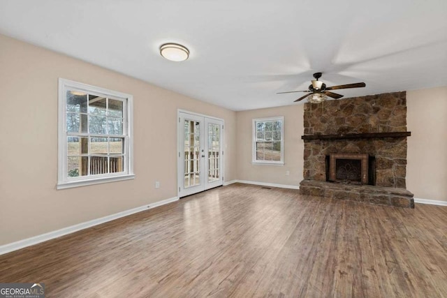 unfurnished living room featuring hardwood / wood-style flooring, a stone fireplace, french doors, and ceiling fan