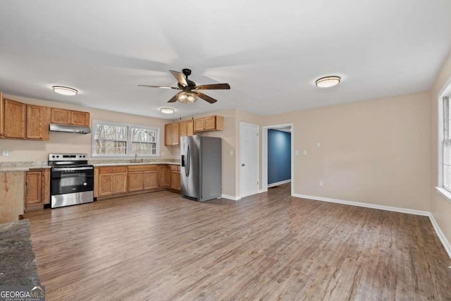 kitchen with sink, hardwood / wood-style flooring, ceiling fan, stainless steel appliances, and light stone countertops