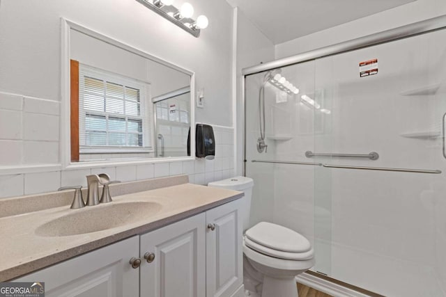 bathroom featuring vanity, toilet, tile walls, and a shower with shower door