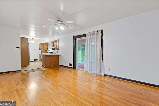 unfurnished living room with ceiling fan, sink, and light wood-type flooring