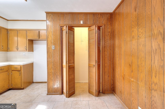 kitchen featuring wood walls, crown molding, tasteful backsplash, light tile patterned floors, and tile counters