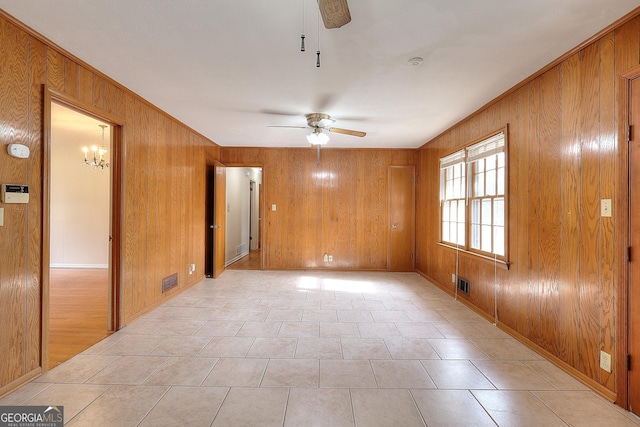 spare room featuring ceiling fan with notable chandelier and wood walls