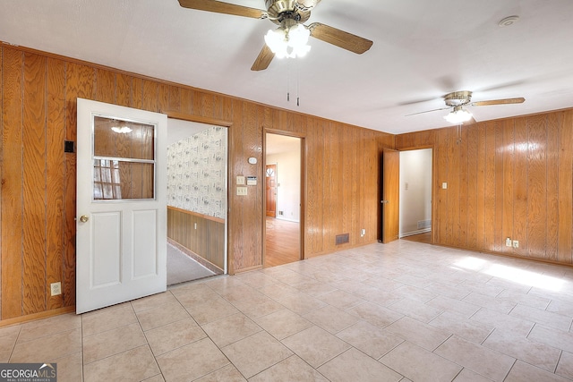 tiled spare room featuring ceiling fan and wooden walls