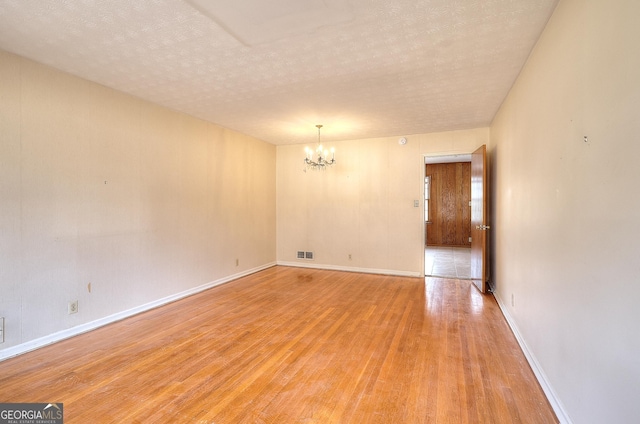 empty room with a textured ceiling, an inviting chandelier, and light hardwood / wood-style flooring