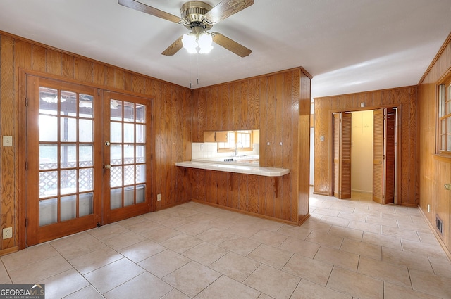 kitchen with french doors, sink, wooden walls, kitchen peninsula, and ceiling fan