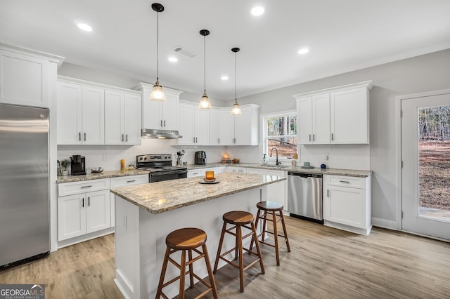 kitchen featuring decorative light fixtures, appliances with stainless steel finishes, a kitchen breakfast bar, a kitchen island, and white cabinets