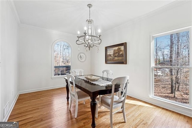 dining area with crown molding, a chandelier, and light hardwood / wood-style flooring