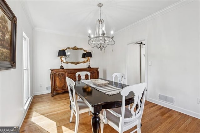 dining area featuring wood-type flooring, a barn door, ornamental molding, and an inviting chandelier