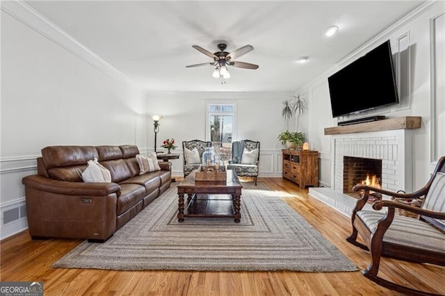 living room with crown molding, ceiling fan, a brick fireplace, and light hardwood / wood-style flooring