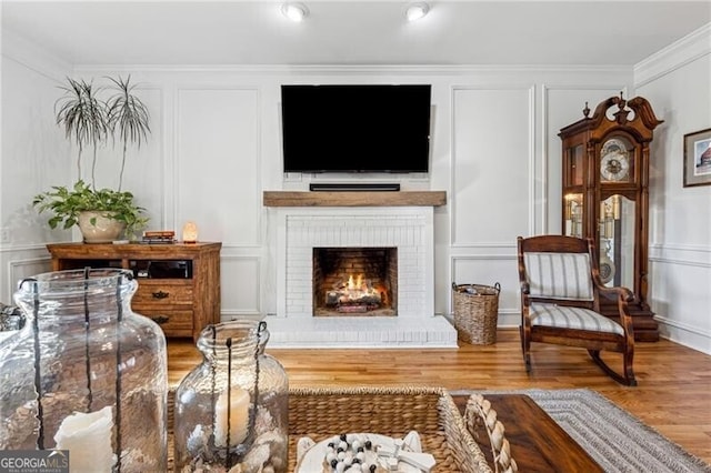 sitting room with a brick fireplace, crown molding, and hardwood / wood-style floors