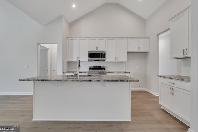 kitchen with white cabinetry, appliances with stainless steel finishes, a center island with sink, and dark stone counters