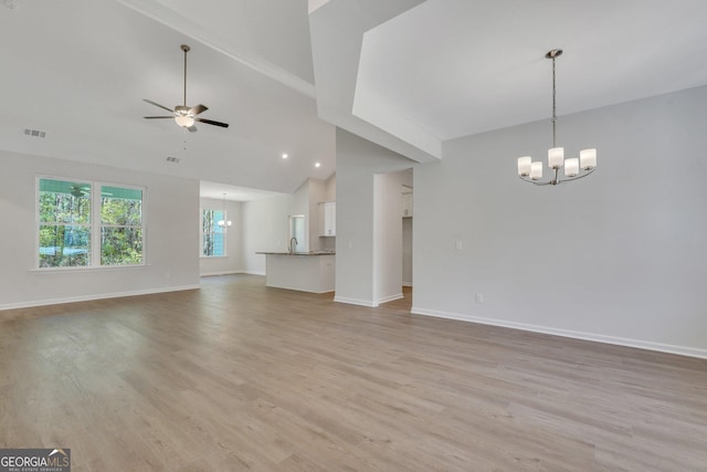 unfurnished living room with ceiling fan with notable chandelier, high vaulted ceiling, sink, and light hardwood / wood-style floors