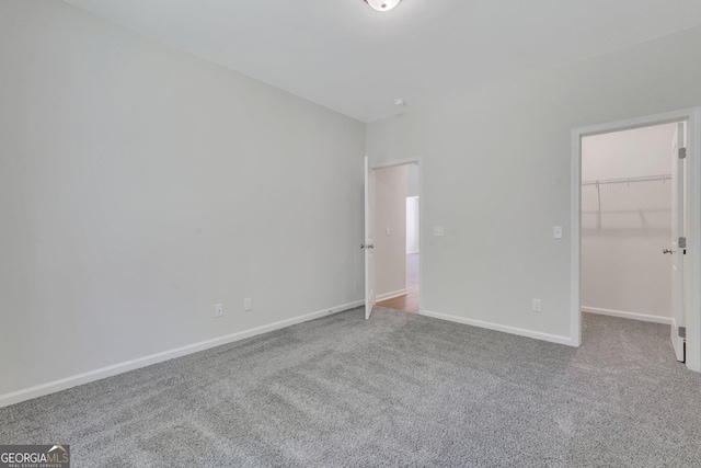 unfurnished bedroom with carpet floors, a walk in closet, and baseboards