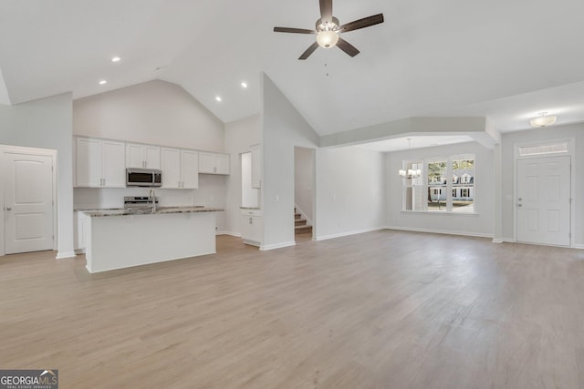 unfurnished living room with high vaulted ceiling, a chandelier, stairs, a ceiling fan, and light wood finished floors
