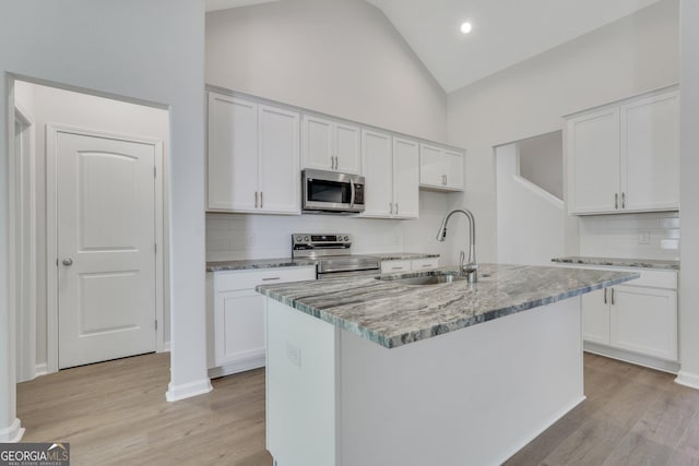 kitchen with sink, white cabinets, light stone counters, stainless steel appliances, and a center island with sink