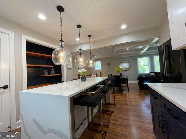 kitchen featuring light stone counters, a center island, hanging light fixtures, dark hardwood / wood-style flooring, and white cabinets