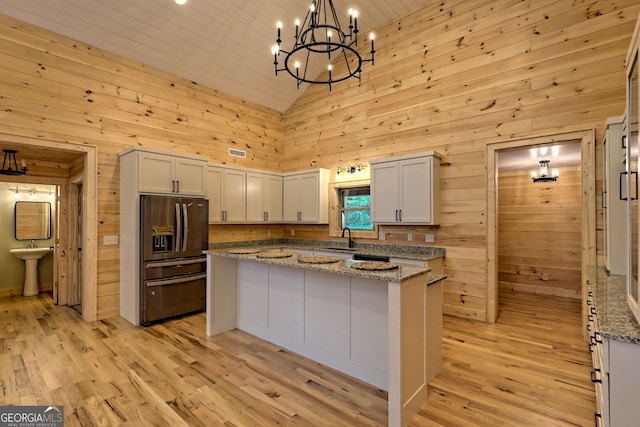 kitchen featuring sink, light stone counters, a center island, refrigerator with ice dispenser, and pendant lighting