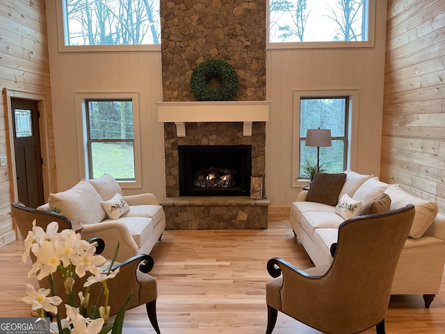 living room featuring light hardwood / wood-style flooring, a stone fireplace, a high ceiling, and wood walls